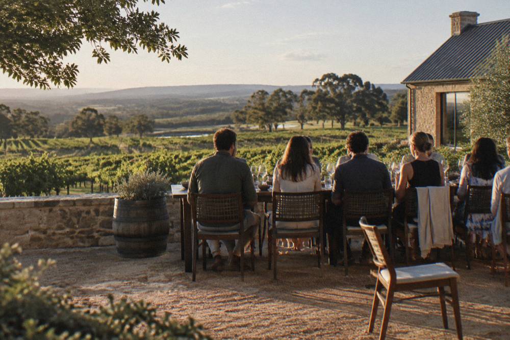 Diners seated at an outdoor winery table with lunches and water glasses on a warm afternoon