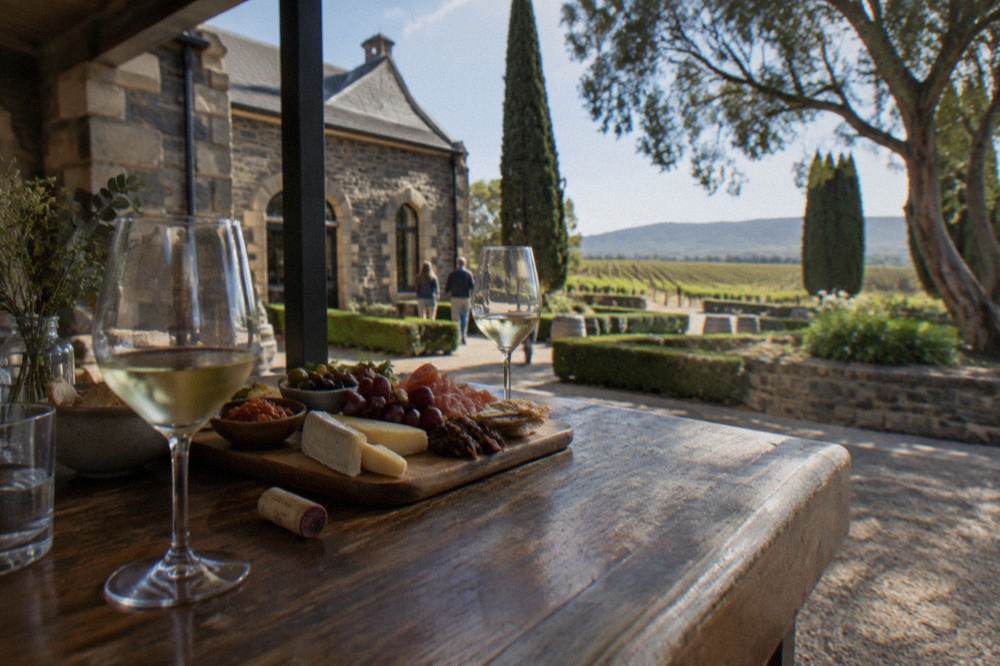 A platter of cheese and tapas beside glasses of white wine on a cellar door bar