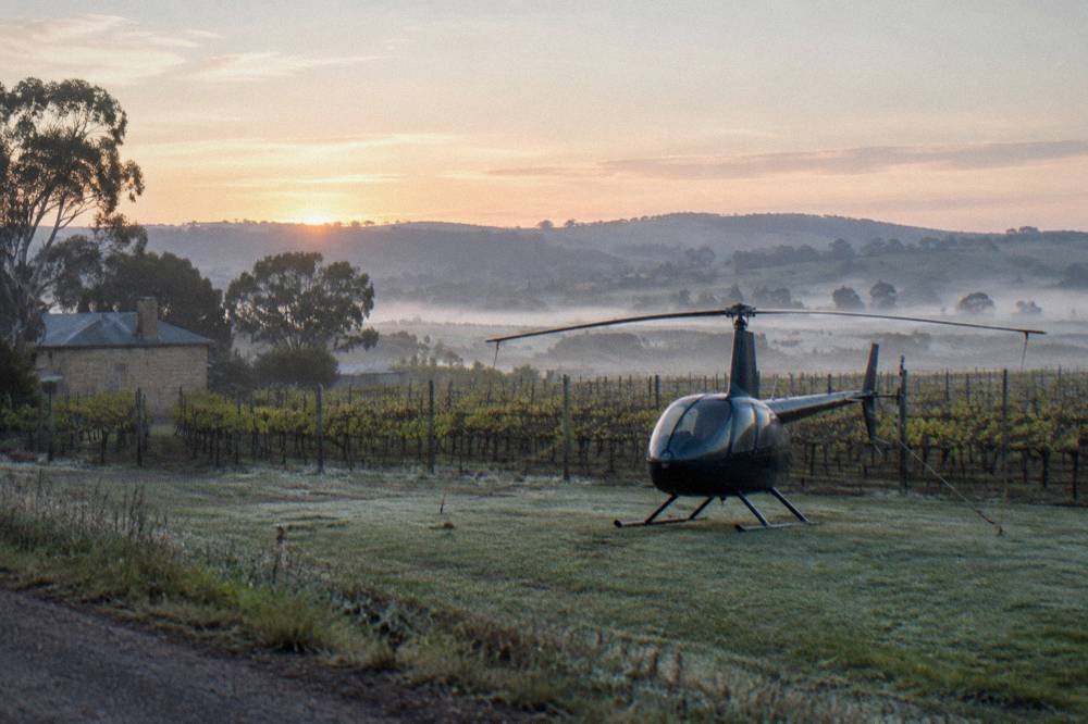 A small helicopter parked on a grass strip beside Barossa vineyards