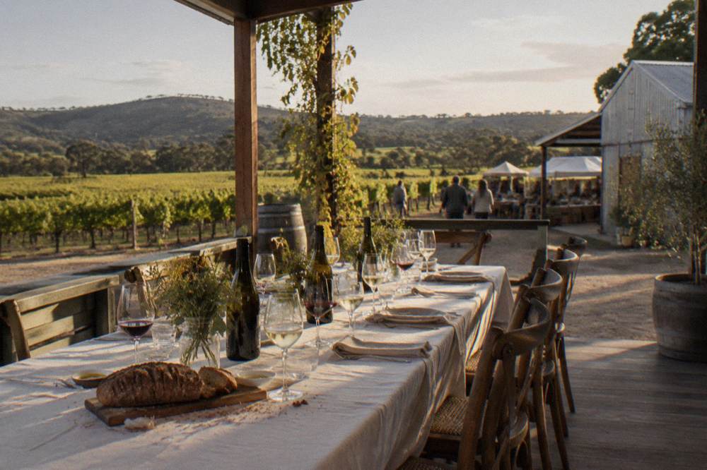 A long table set for lunch on a winery veranda overlooking terraced vineyards in late afternoon light