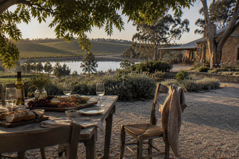 A shaded outdoor table set with a regional platter, bread and wine glasses