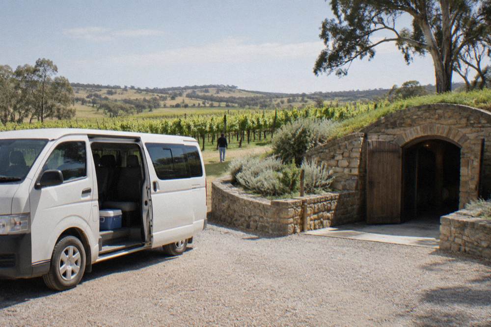 A small tour van parked outside a stone cellar door in the Barossa