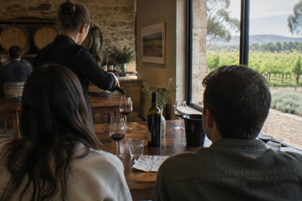 A guide pouring red wine for guests seated at a wooden tasting table