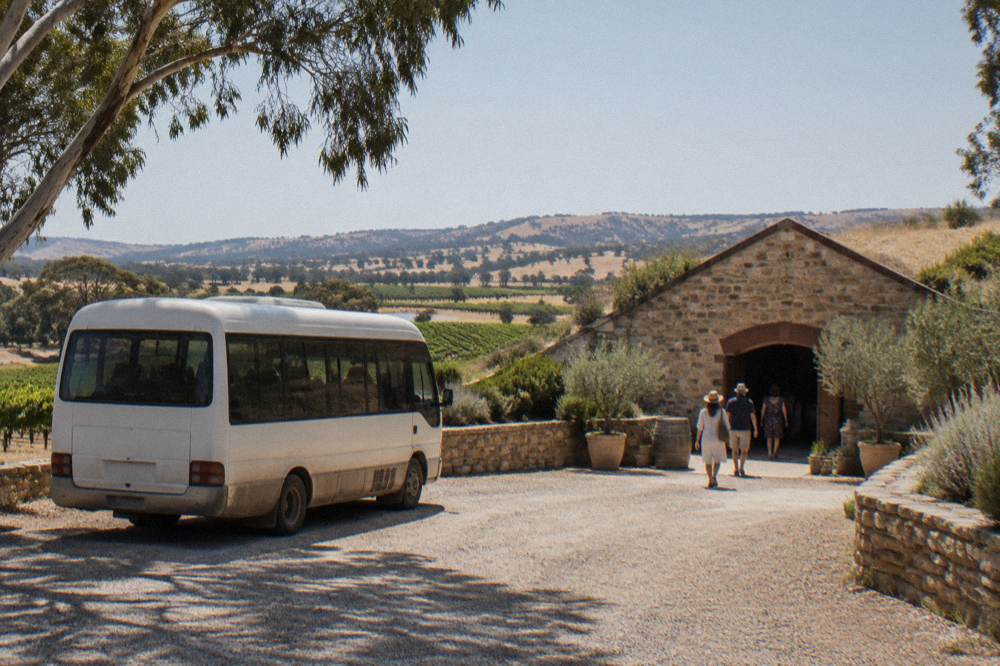 A small tour van parked on a gravel drive beside a cellar door entrance