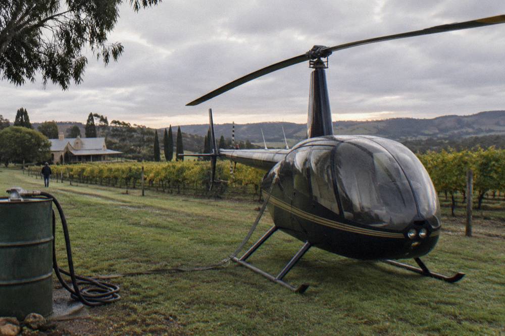 A small helicopter parked on a grassed pad beside vineyards near Lyndoch