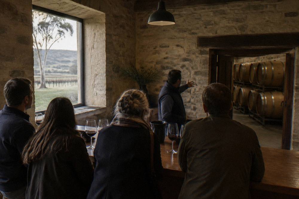 A small group of people tasting wine at a cellar door with a guide explaining the wine.