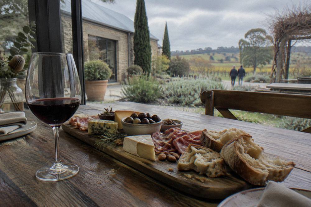 A table set with a regional platter of cheese, charcuterie and bread alongside a glass of red wine with vineyards beyond