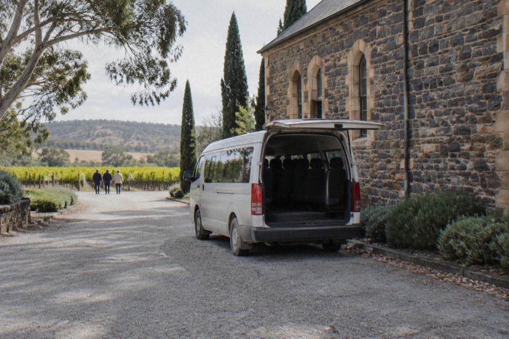 A small tour van parked on a gravel drive beside a stone winery building