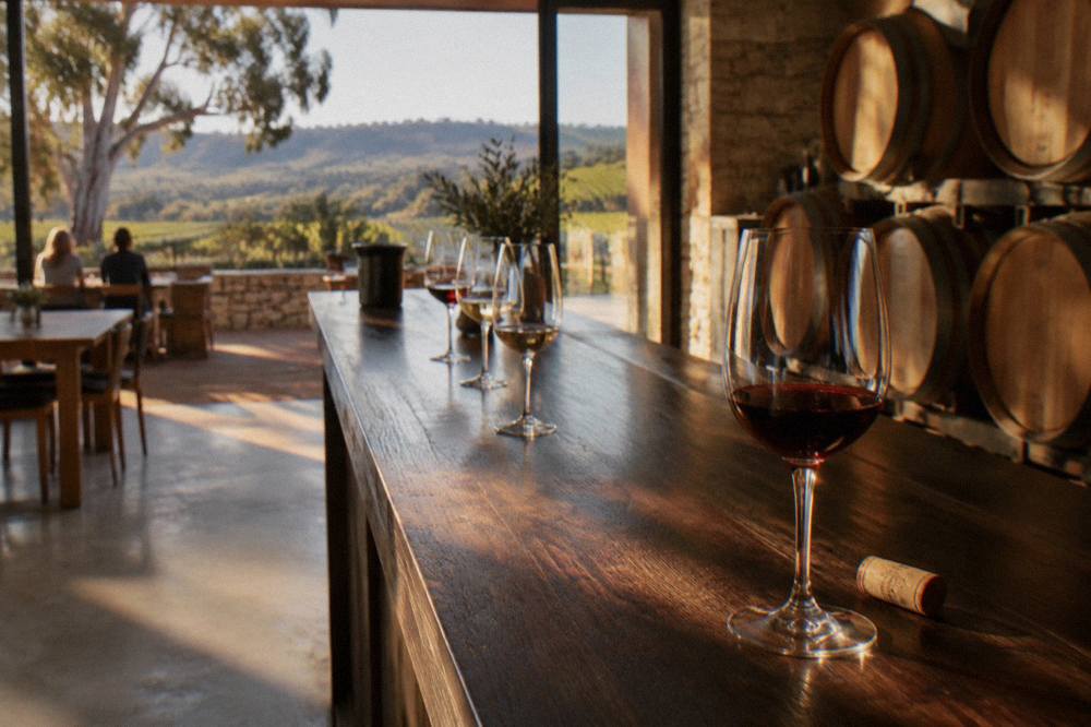 Cellar door tasting glasses filled with red wine on a wooden bar with barrels behind