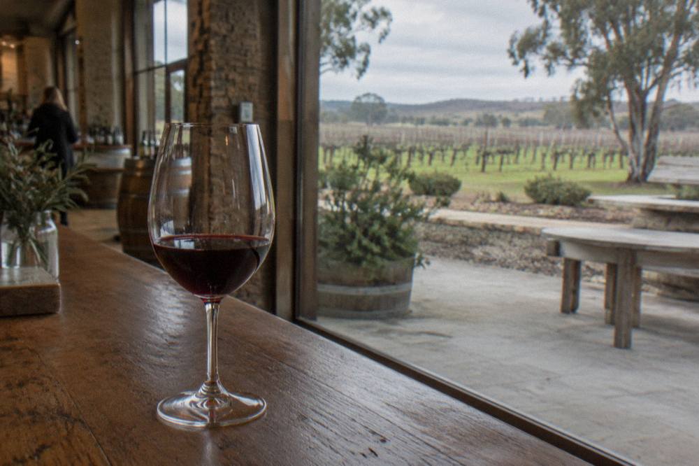 A tasting glass of red wine resting on a timber bar top inside a cellar door