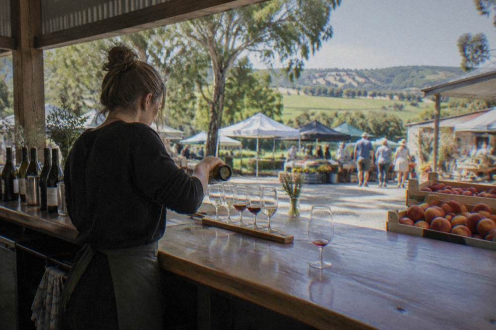 A cellar door host pouring a tasting flight behind a timber bar