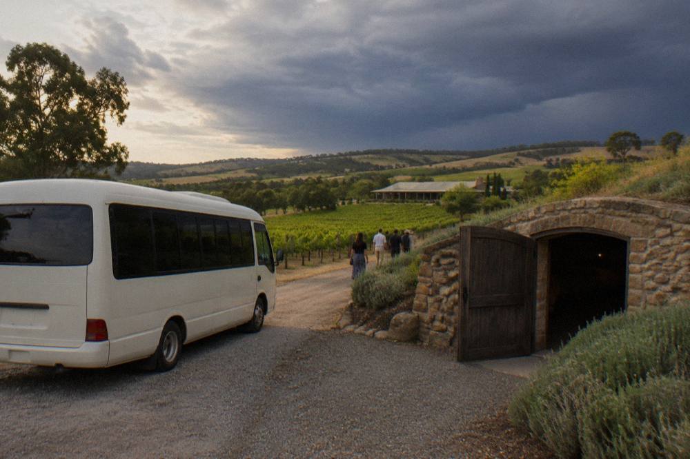 A small tour van parked beside a stone cellar door among vineyards