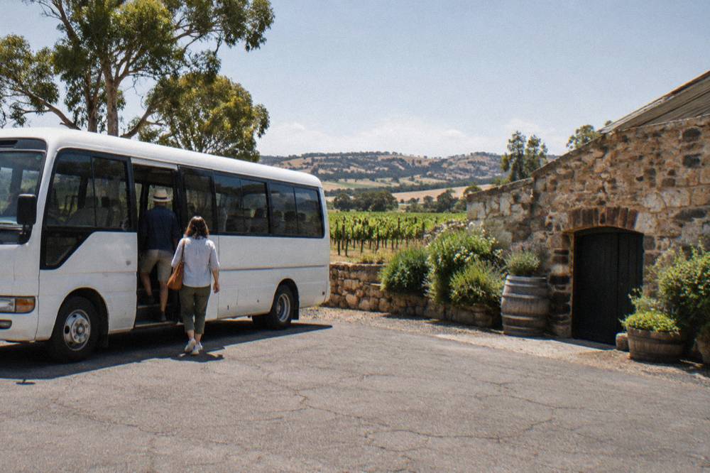 A hop-on hop-off bus parked outside a stone cellar door with passengers boarding