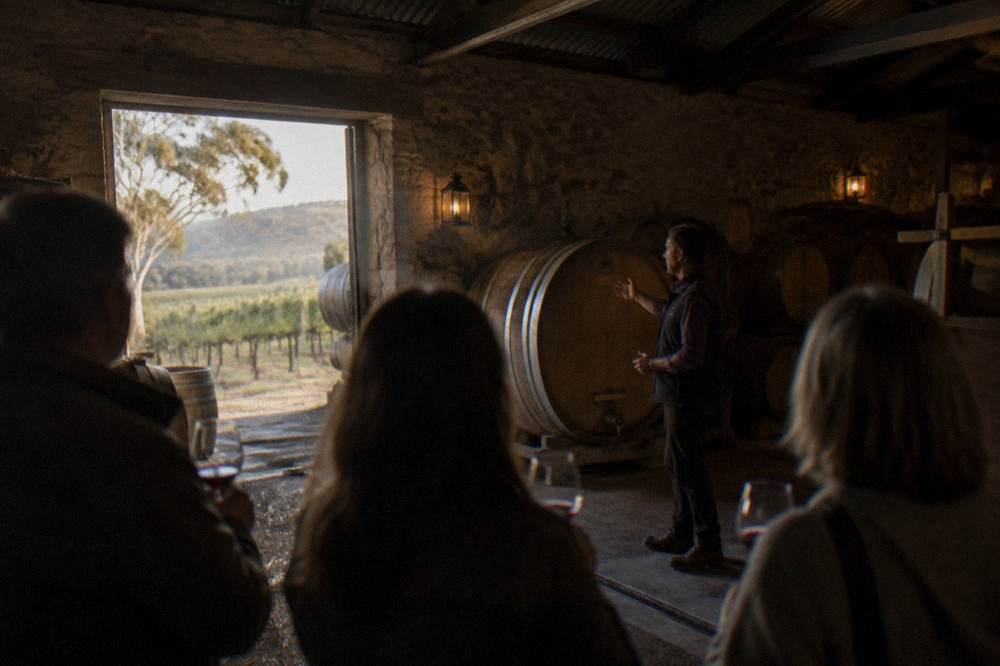 A small group of people tasting wine at a cellar door with a winemaker explaining the wine