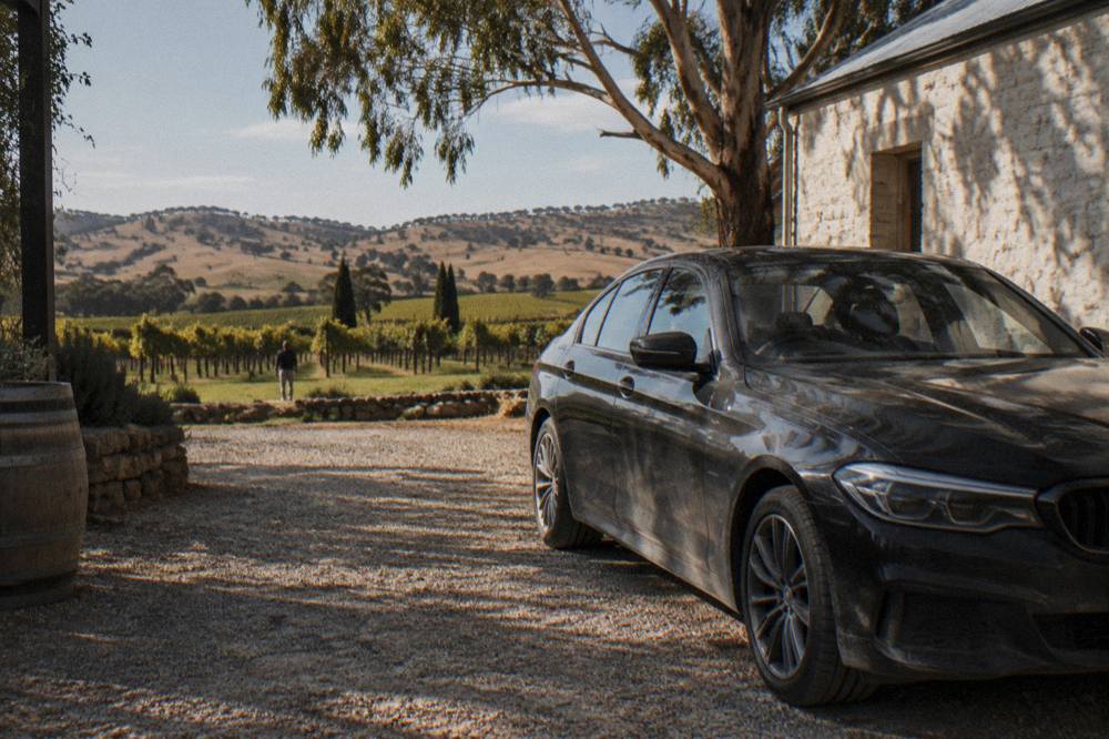 A luxury sedan parked on a gravel drive beside a stone winery building