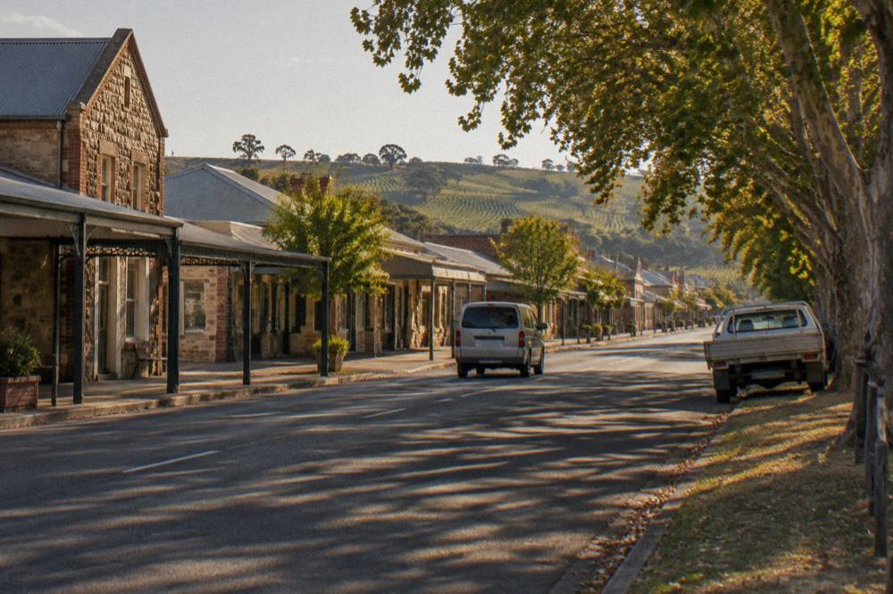 A compact tour van driving along a quiet country road lined with vineyards and old stone buildings