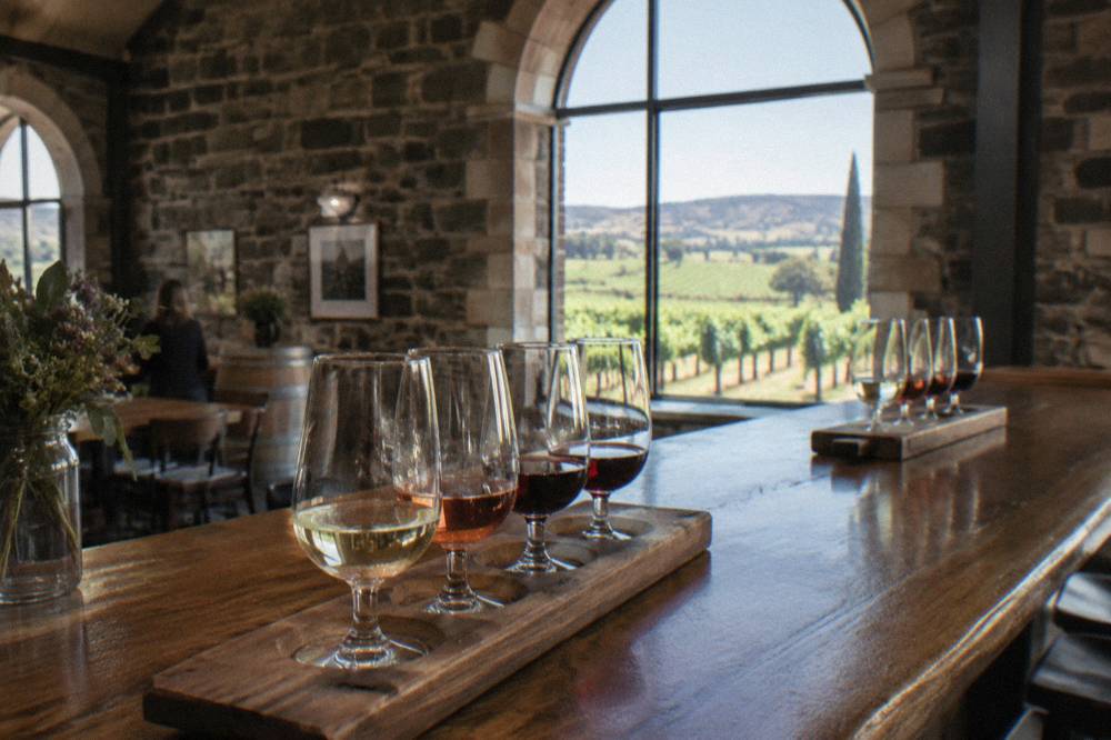 Wooden tasting flight glasses lined along a cellar door bar with vineyard views through the window