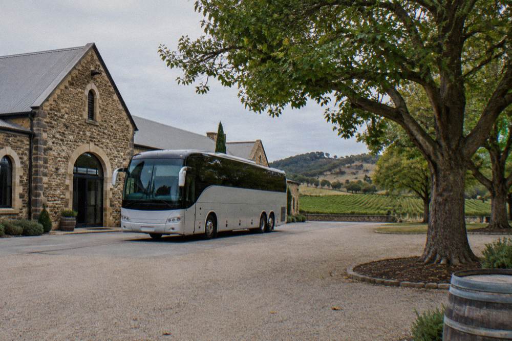 A large touring coach parked beside a heritage stone winery building with a crowd-free courtyard