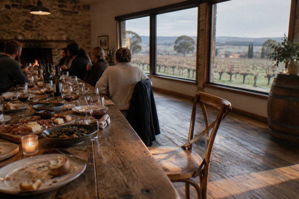 A long shared lunch table set with regional platters, bread and wine glasses inside a rustic winery dining room