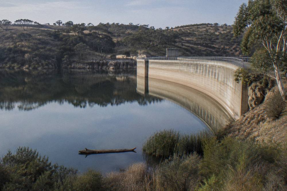 Curved concrete dam wall of the Barossa Reservoir reflected in still water