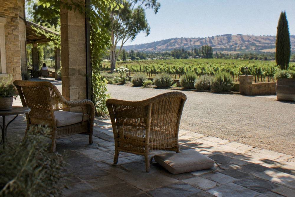 A shaded cellar door verandah with chairs overlooking vineyard rows at midday
