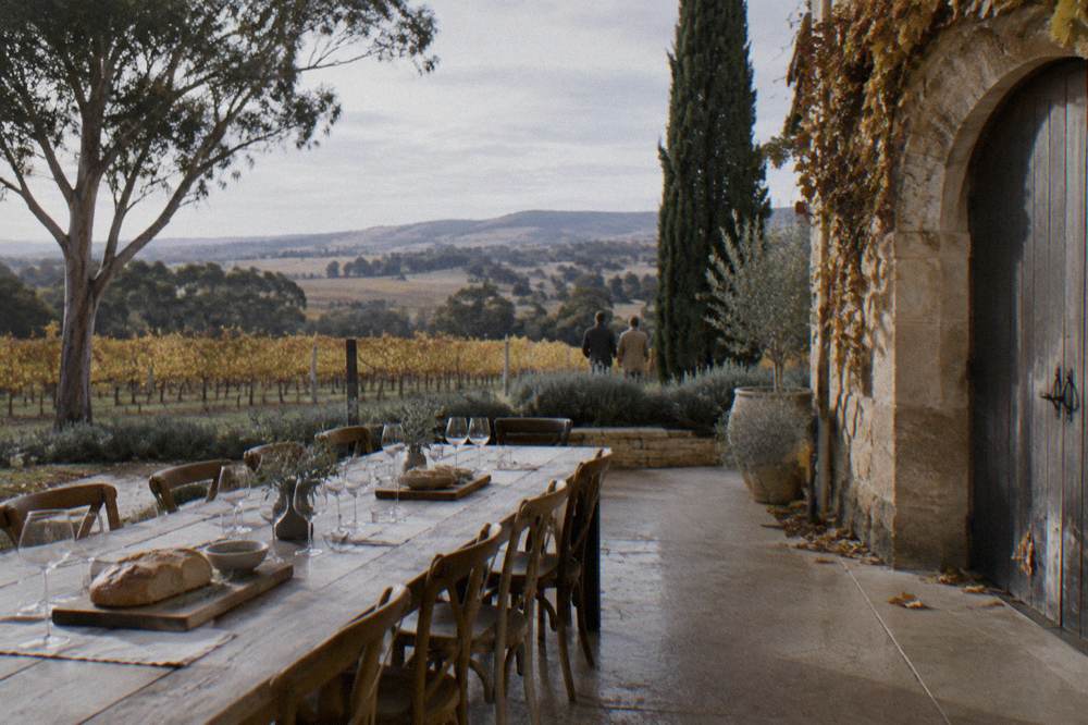 Long wooden table set for lunch beside a cellar door with vineyard views